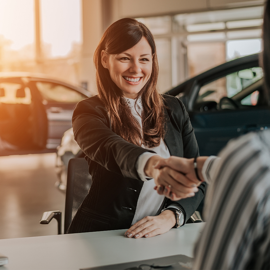 Dealership employee smiling shaking hands with satisfied customer.
