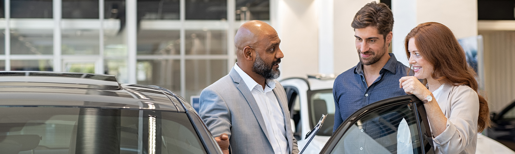 Dealership employee showing customers cars on showroom floor.