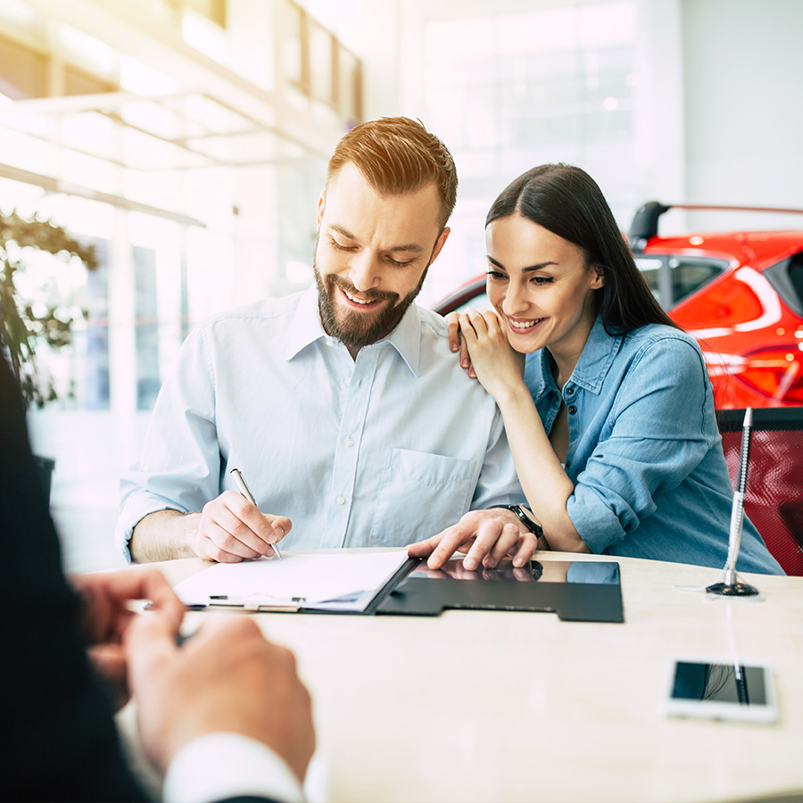 Beautiful happy couple sitting at the table signing a documents for the purchase of a car at the dealership