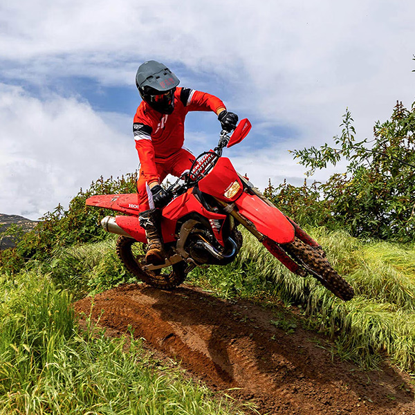 CRF450X shown riding through a grassy hill with dirt