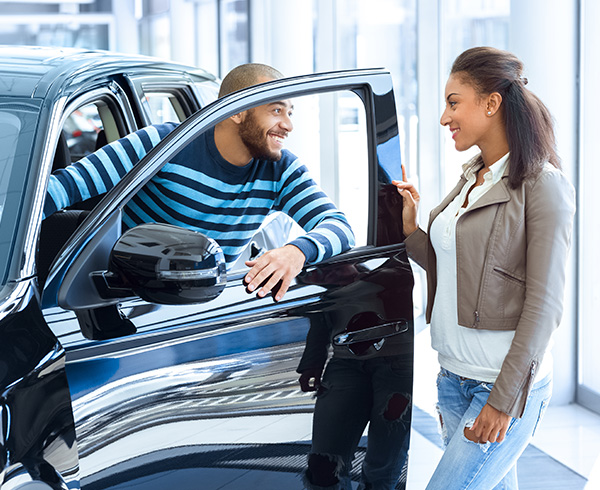 Two customers checking out car in dealership showroom smiling at one another