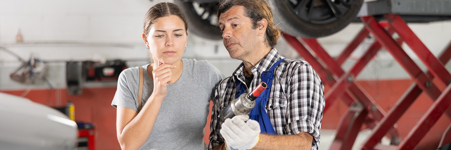 Service customer thinking while looking at her vehicle with a mechanic standing next to her