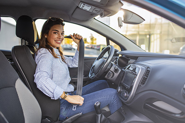 Woman fastening seatbelt in car, smiling.