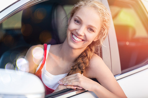 Young woman smiling, looking out of a car window with sunlight and bokeh