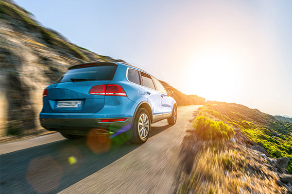 Blue SUV driving on mountain road rear three quarter image