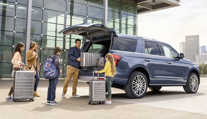 A family unloads luggage from a 2023 Ford Expedition SUV parked in front of an urban building