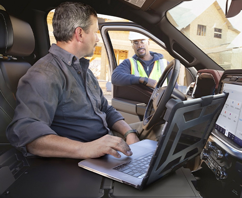 A person in a parked 2022 Ford F-150 using his laptop