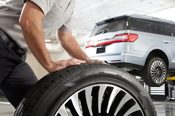 Male mechanic hold and rolling tire at repairing service garage background.