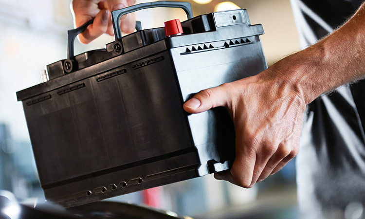 Closeup of a MINI Service Technician loading a MINI Original Battery under the hood of a MINI vehicle in a MINI Service Center.