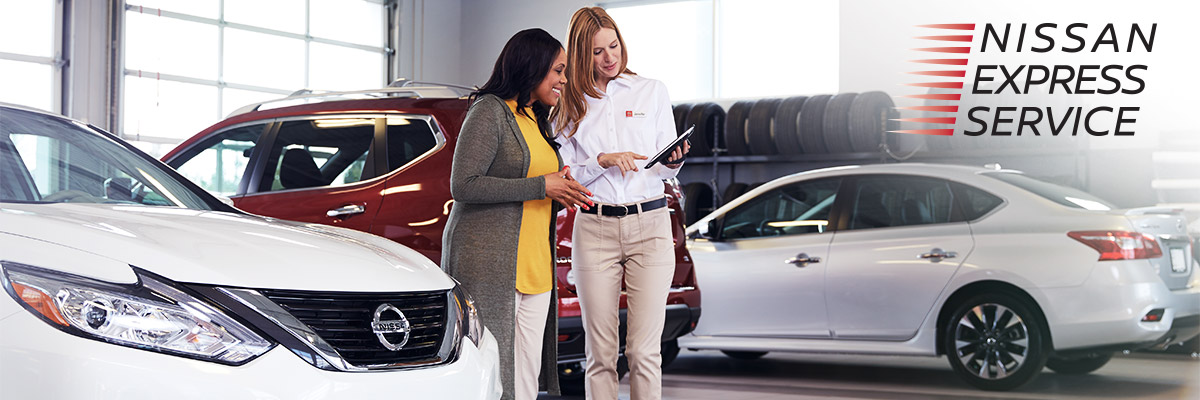 Two people standing in a Nissan body shop with the Nissan Express Service Logo