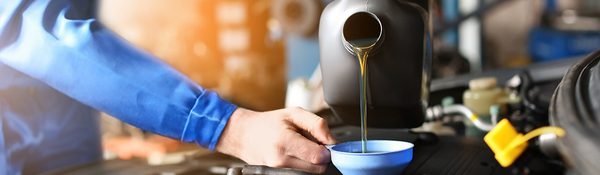 Mechanic pouring oil into car engine for maintenance.