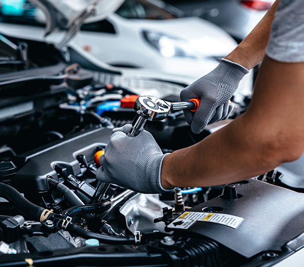 Mechanic using wrench while working on car engine at garage workshop.