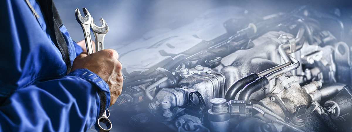 Mechanic holding wrenches with a car engine in the background.