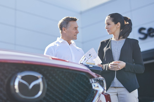 Mazda employee talking over service papers with customer outside of service center