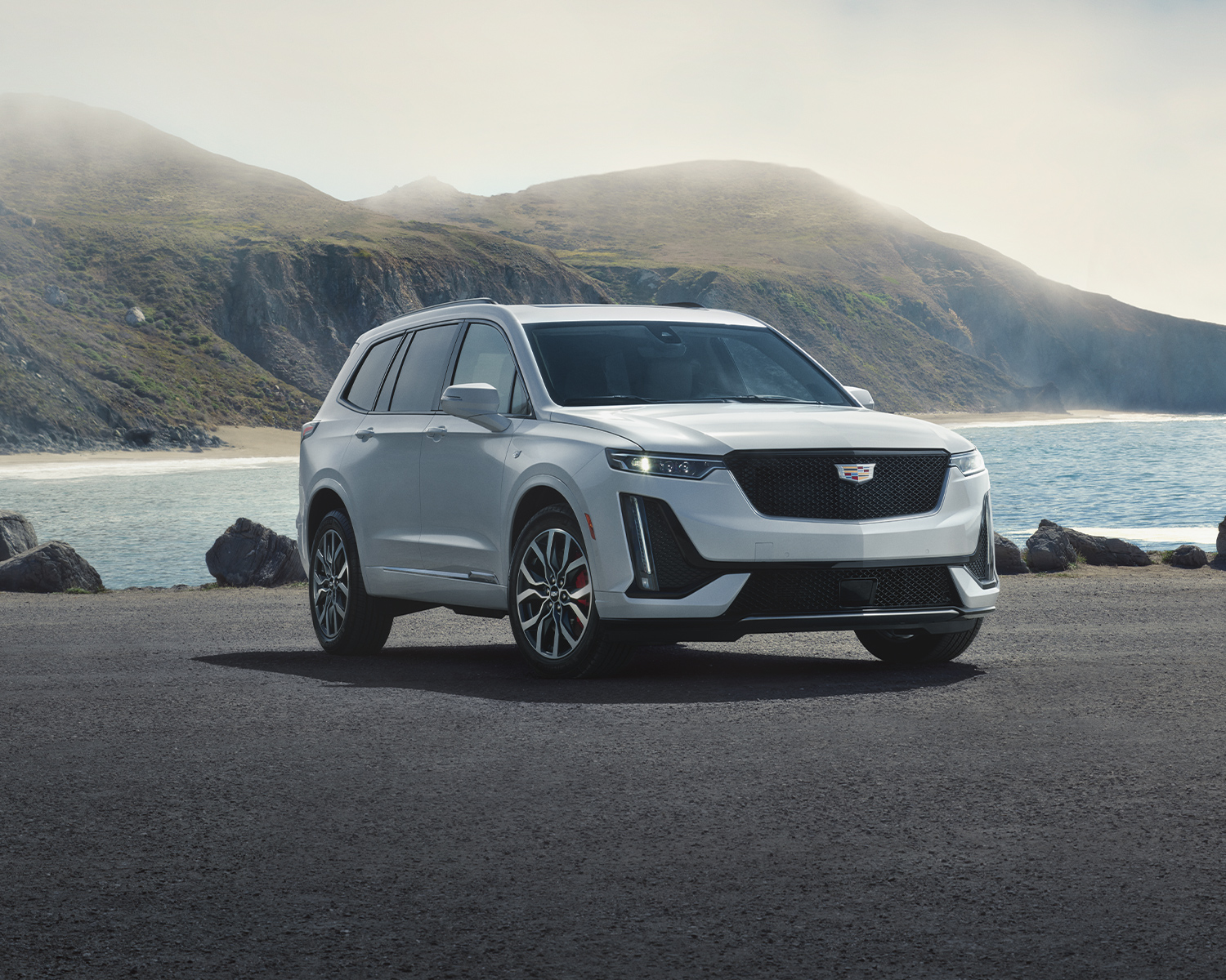 3/4 view of a 2024 Cadillac XT6 parked with ocean and mountains in the background