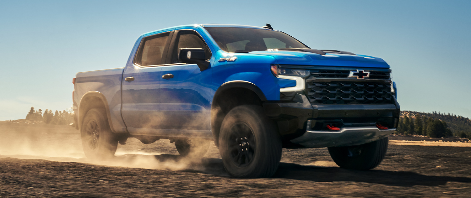 A blue 2025 Chevrolet Silverado 1500 offroading with trees in the background