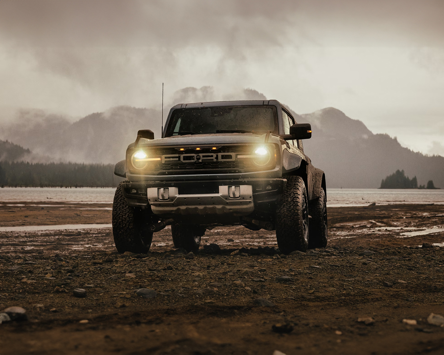 2025 Ford Bronco parked offroad with its headlights on with the mountains in the background