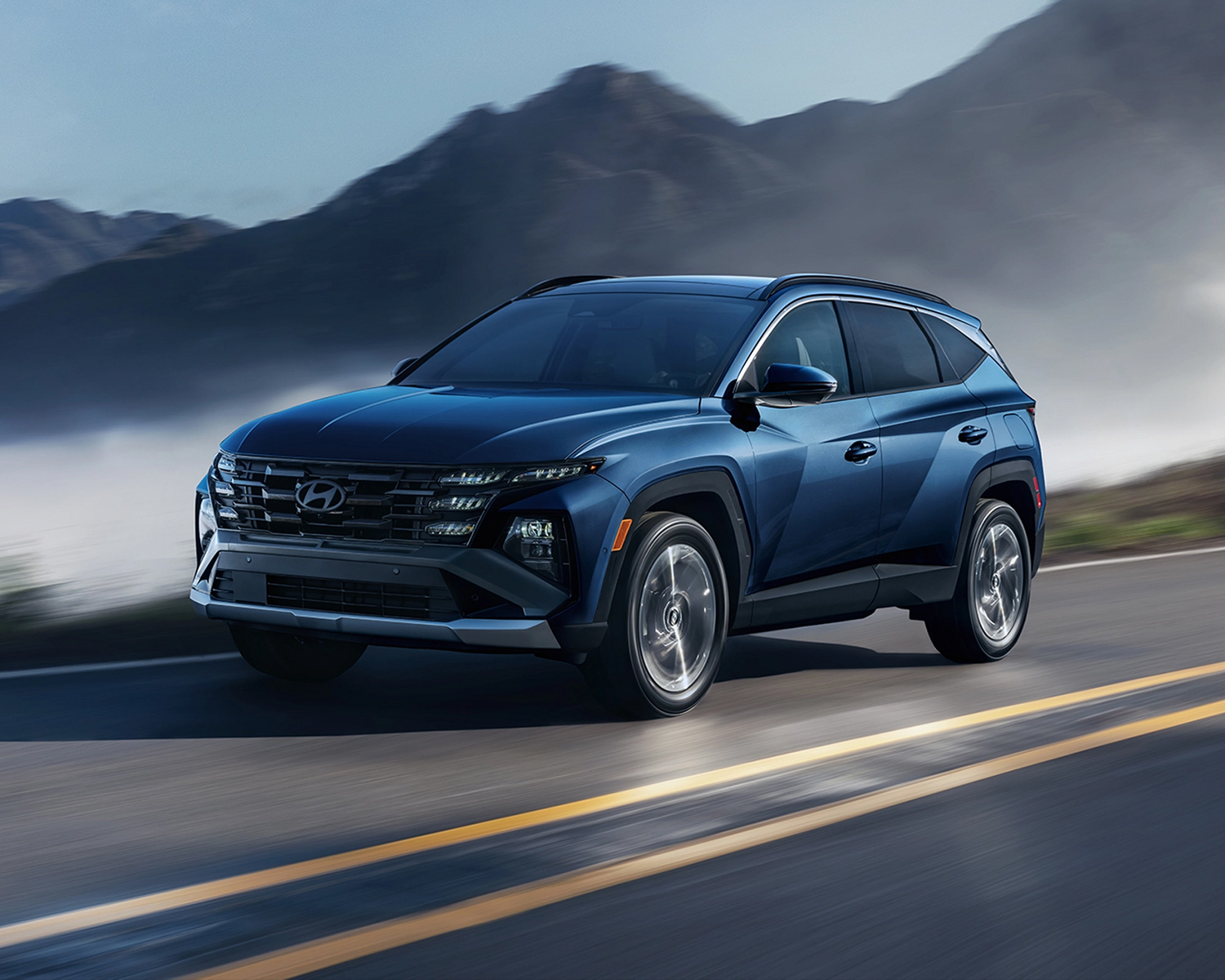 2025 Hyundai Tucson driving on a road with mountains behind it