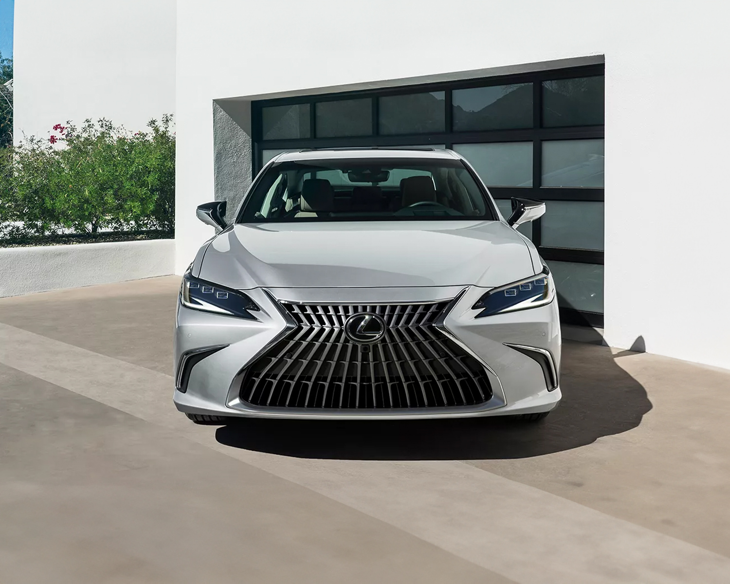 Front view of a silver 2025 Lexus ES parked in front of a modern garage.