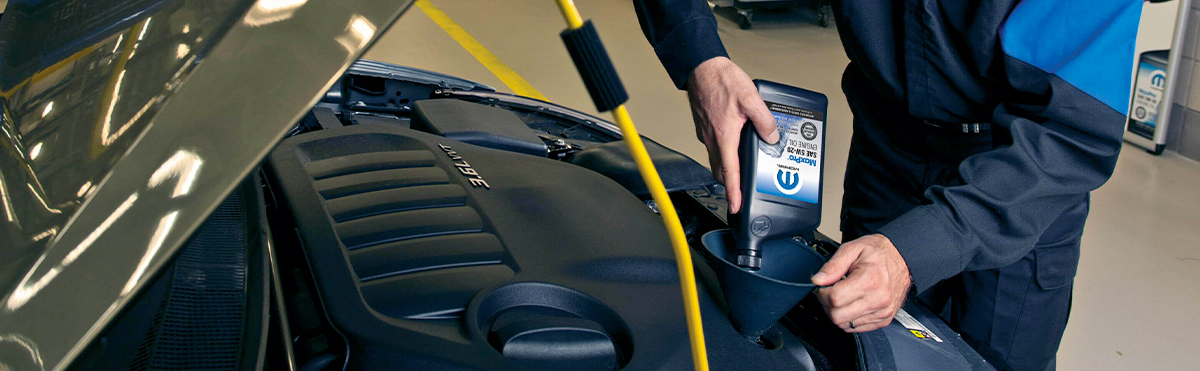 View of an assistant performing an oil change in a car with the hood open.