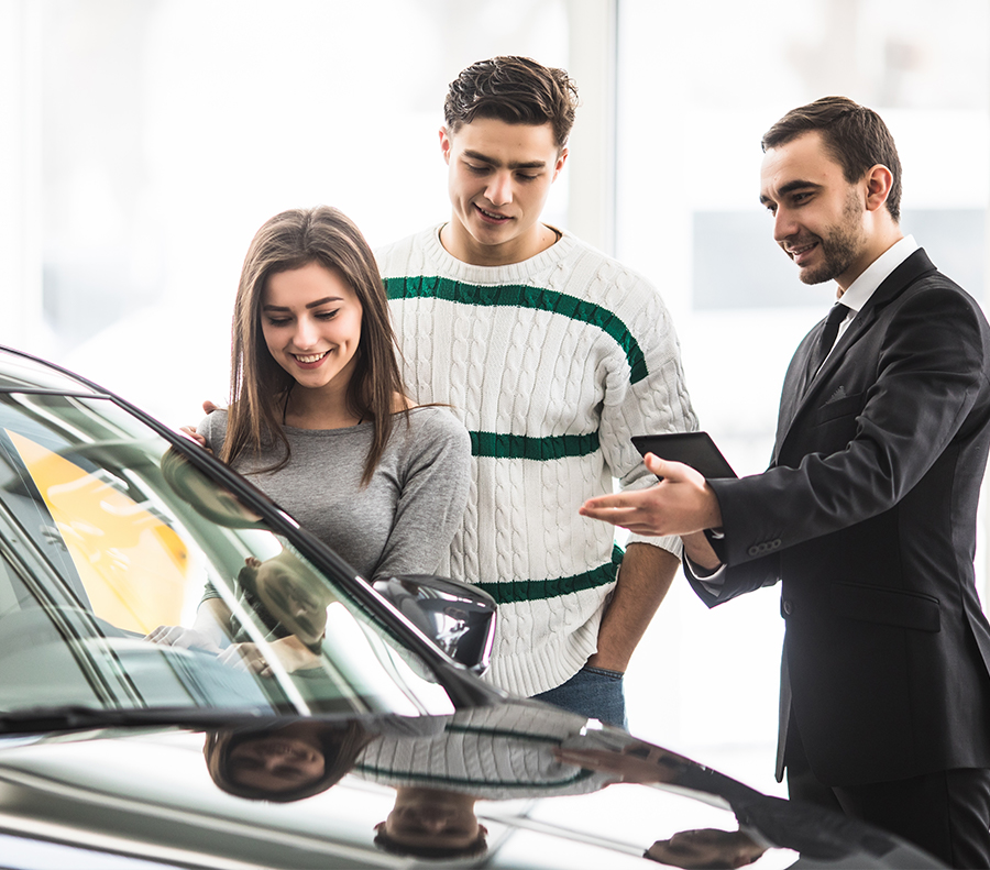 salesperson showing customers a new car at a dealership