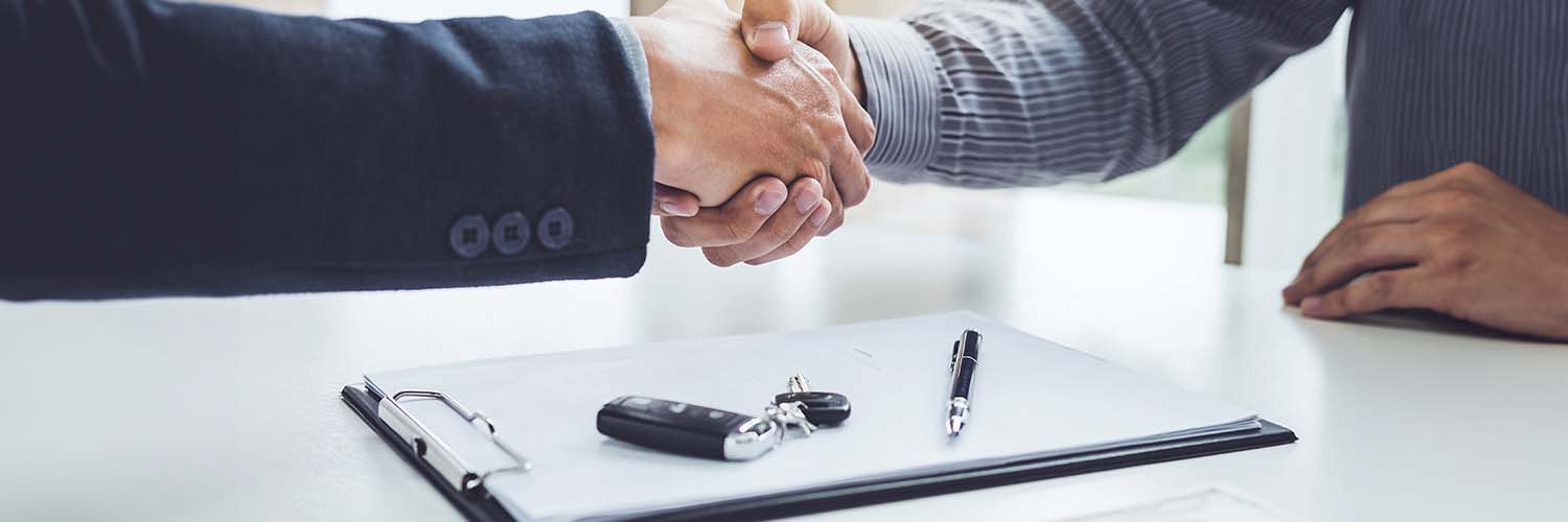 close up of people shaking hands with a contract and car keys shown
