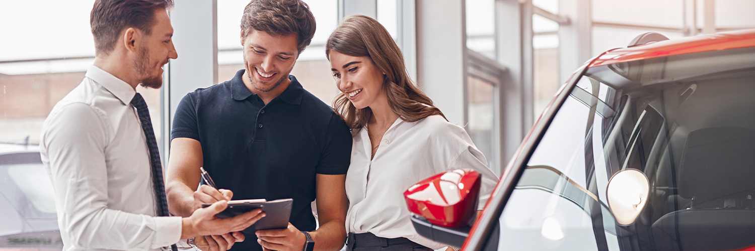 Delighted couple and manager signing papers in car dealership