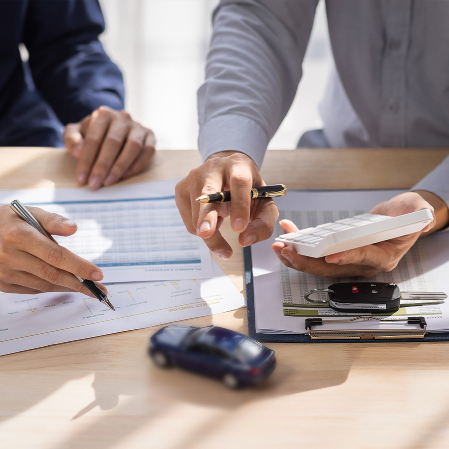 Person signing car purchase agreement with keys and toy car on desk