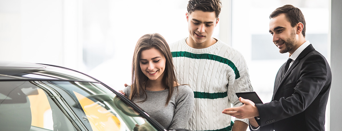 Customers smiling looking at car being shown to them by dealership employee