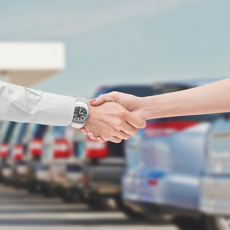 two people shaking hands with car lot in the background