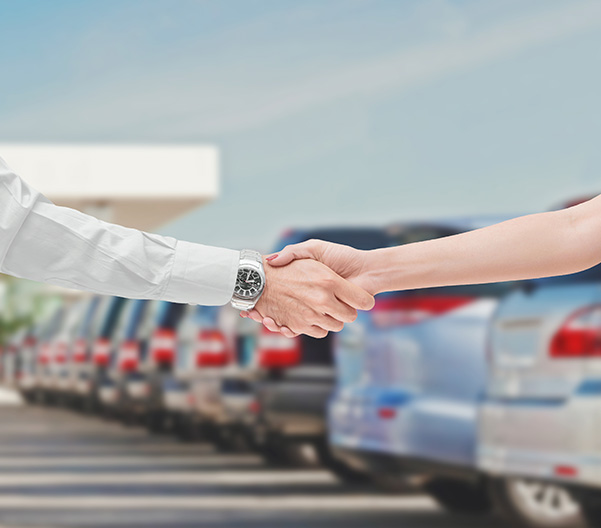 two people shaking hands with car lot in the background