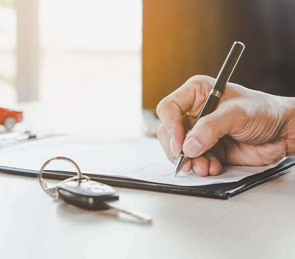close up of someone signing a contract with car keys in sight