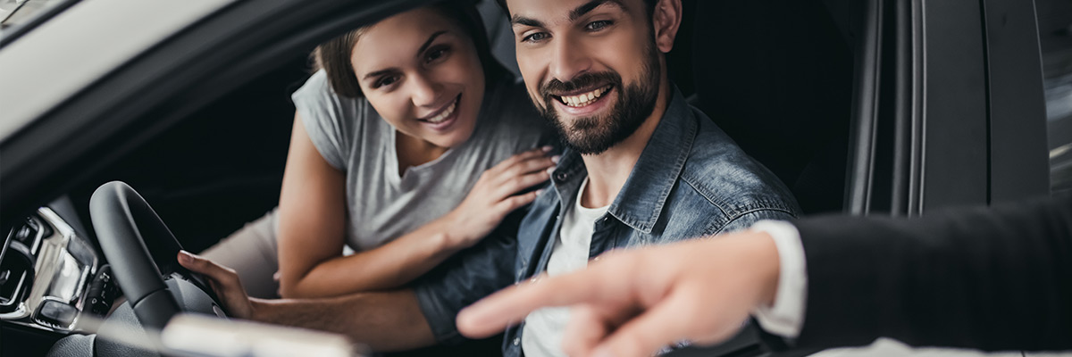 Man and woman sitting in car being shown details by salesman