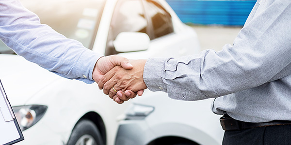 two people shaking hands on a car lot