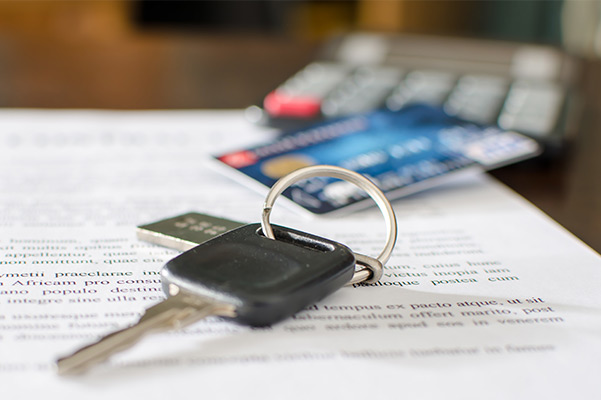 Car keys sitting on a pile of paperwork with a credit card and calculator blurred out in the background