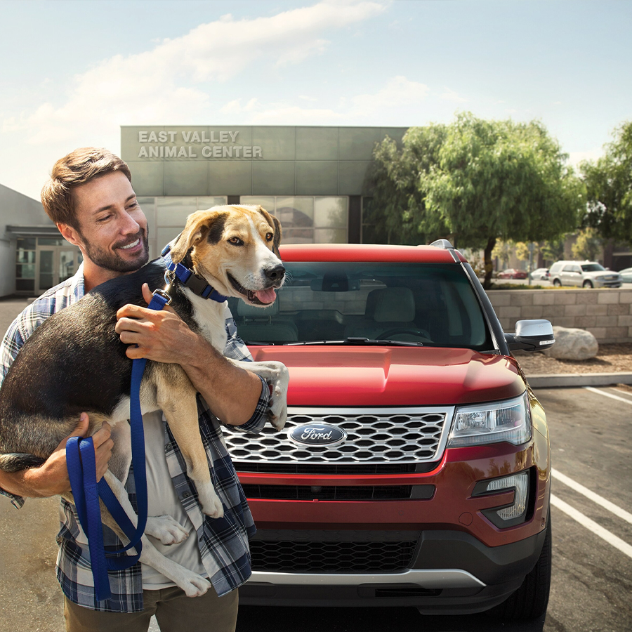 Person holding a dog standing in front of a parked Ford SUV