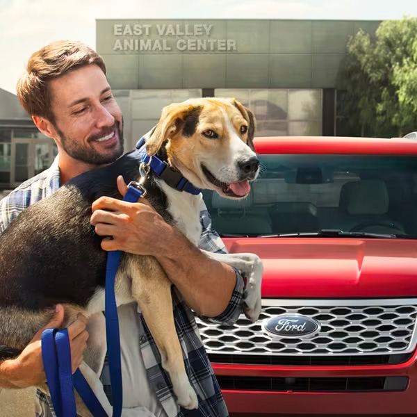 Person holding a dog standing in front of a parked Ford SUV