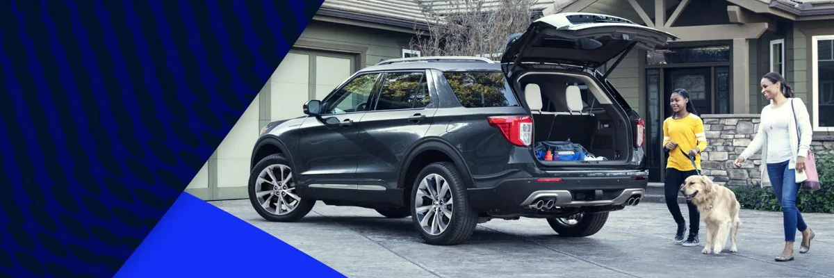 Two people and a dog approach the rear open hatch of a Ford Explorer® SUV parked in a driveway