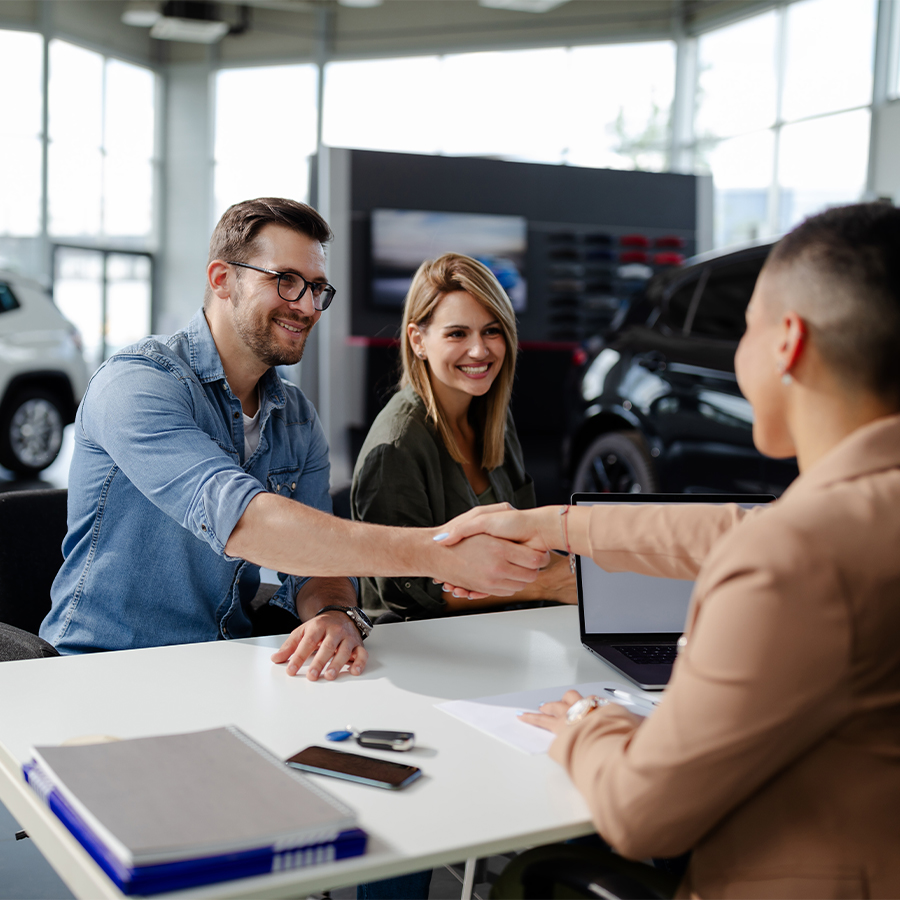 Customers shaking hands with a Subaru dealership representative in a showroom