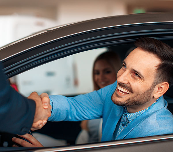 Dealership employee smiling shaking hands with satisfied customer.
