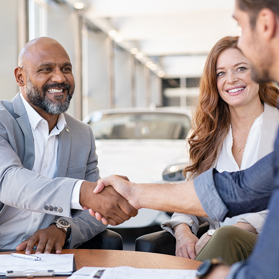 Dealership employee smiling shaking hands with satisfied customer.