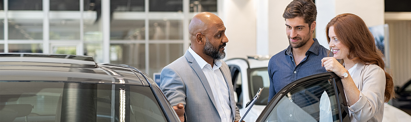 Dealership employee showing customers cars on showroom floor.